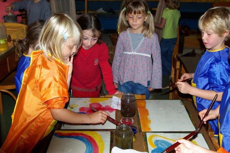 Kindergartenkinder malen mit Aquarellfarben an kleinen Tischen