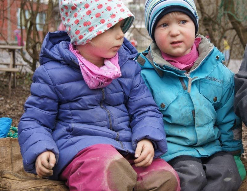 Zwei Kinder sitzen in Winterjacken draussen beieinander